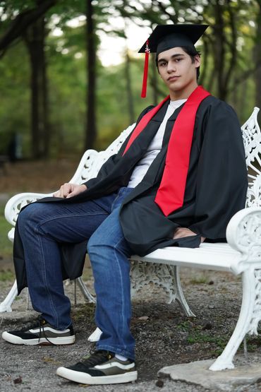 Charleston senior sitting on white garden bench in cap and gown outdoors