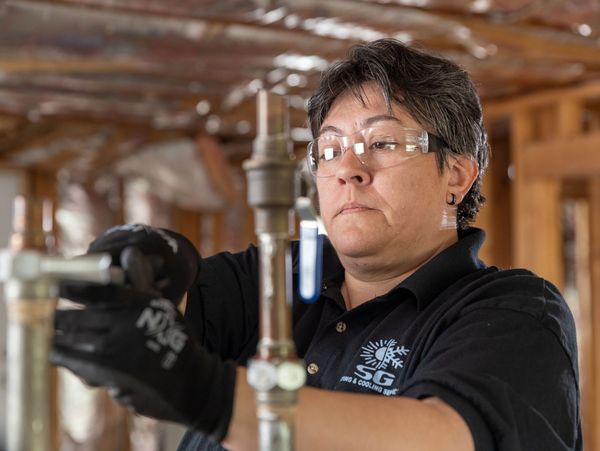 Technician adjusting pipes in an unfinished building with safety glasses and gloves.