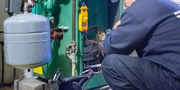 Technician inspecting and testing a heating system with a multimeter.