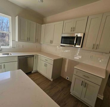Modern kitchen with white cabinets, stainless steel appliances, and wood flooring.