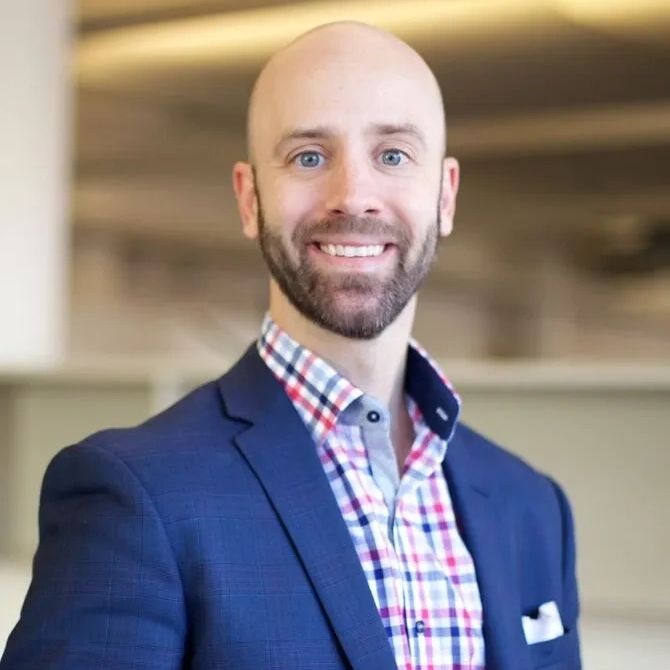 Smiling bald man in a blue suit and checkered shirt.