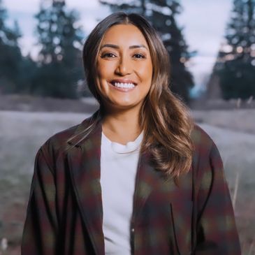 Smiling woman outdoors wearing a plaid jacket and white shirt.