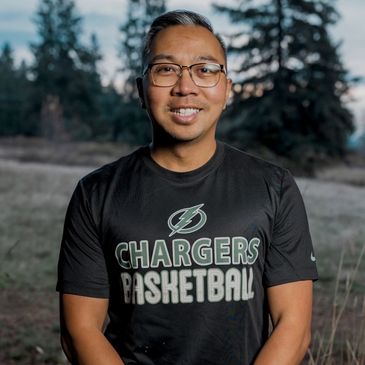 Man wearing a Chargers Basketball t-shirt outdoors with trees in the background.