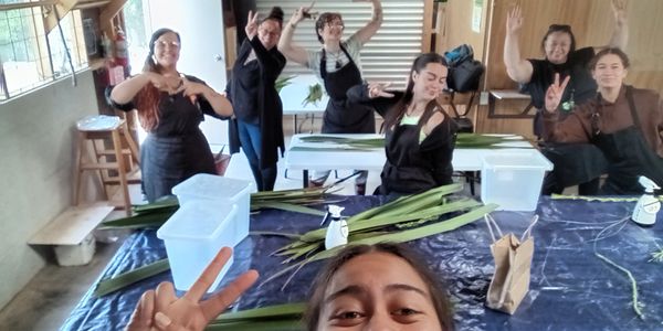 A group of six people posing cheerfully in a workshop setting with green leaves on the table.