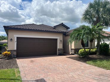 Single-story house with a brown tiled roof and a double garage under a partly cloudy sky.