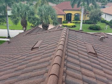 Roof view with palm trees and a yellow house in the background under a cloudy sky.