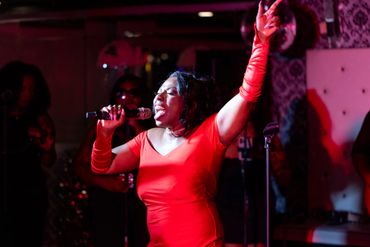A woman passionately singing on stage in a vibrant red dress and gloves.