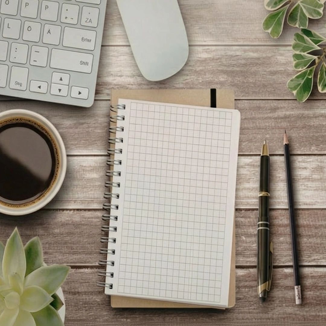 Workspace with a keyboard, mouse, coffee, notebook, pen, pencil, and plants on a wooden table.