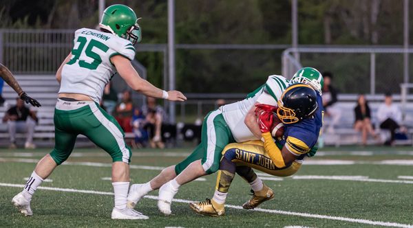 Football player from Saint John tackled by two opponents in green and white.