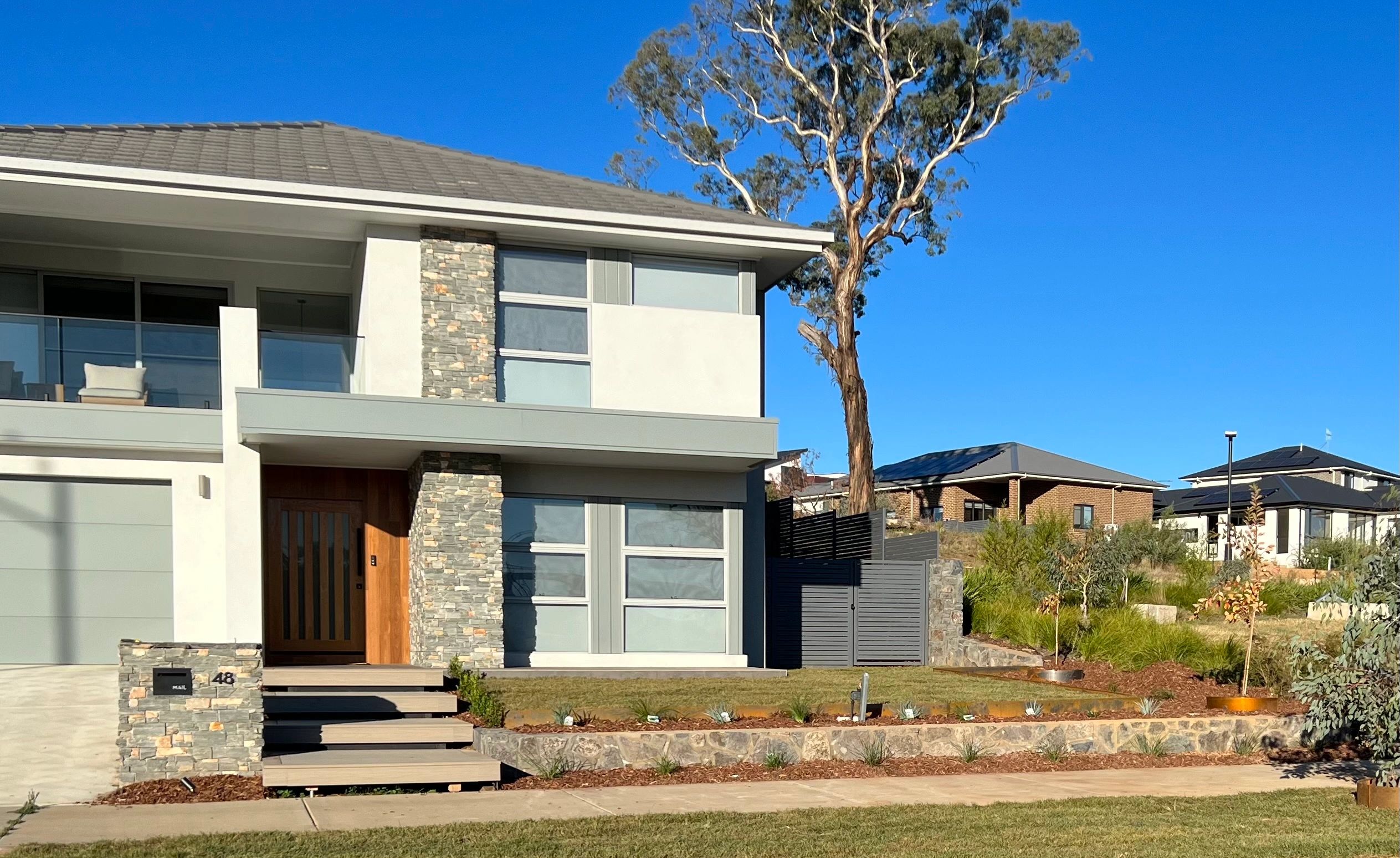 Modern two-story house with stone accents and a tall tree in the front yard.