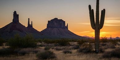 Sunset over a desert landscape with towering rock formations and a tall cactus.