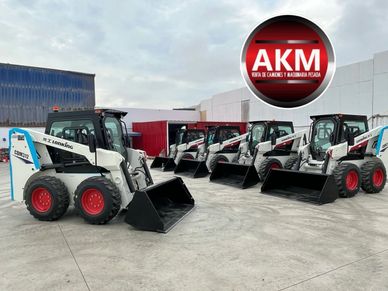 A row of white skid steer loaders parked outside a warehouse.
