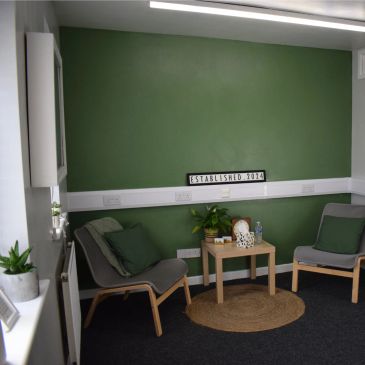 Cozy green-walled waiting area with two chairs and a small table.