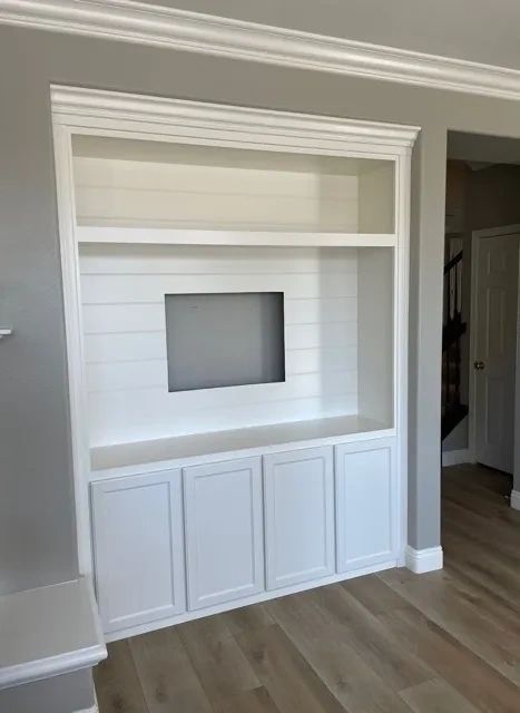 Recessed built-in entertainment center with horizontal shiplap backing and shaker style cabinetry.
