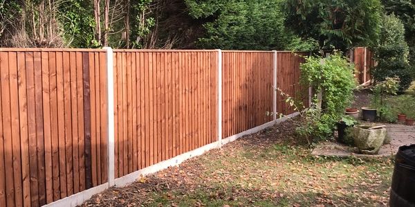 New wooden fence along a backyard with autumn leaves scattered on the ground.
