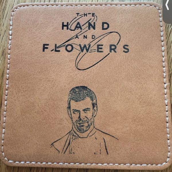 Leather coaster with 'The Hand and Flowers' logo and a chef illustration.