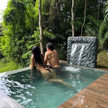 Couple enjoying a private pool with a waterfall in a lush forest setting.