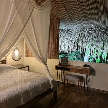 Cozy bedroom with canopy bed and rustic wooden desk under a thatched roof.