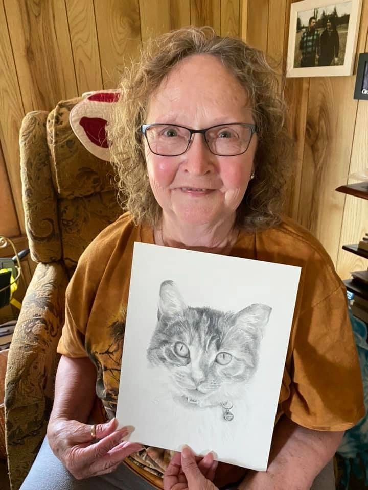 A woman holding a graphite custom cat pet portrait by Linda's Pet Portraits for free during lockdown.