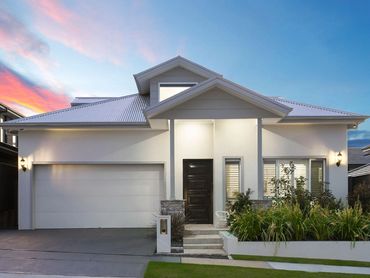 Modern white house with a large garage and well-maintained garden at sunset.