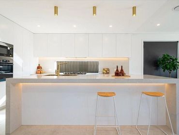 Modern white kitchen with gold accents and two wooden stools at the island.