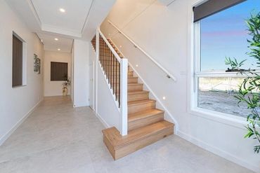Modern hallway with wooden stairs and large window letting in natural light.