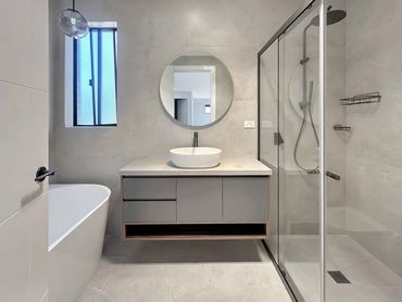 Modern bathroom with floating vanity, round mirror, bathtub, and glass shower enclosure.