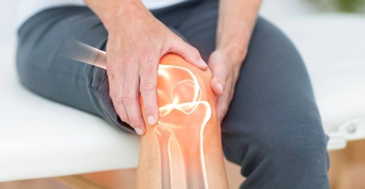A patient sits on a physio treatment table and holds their knee while a stylised image of their joints shows through