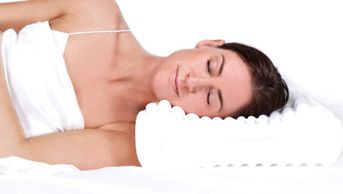 A woman wearing a white top sleeps on her side with her head on a contoured memory foam pillow