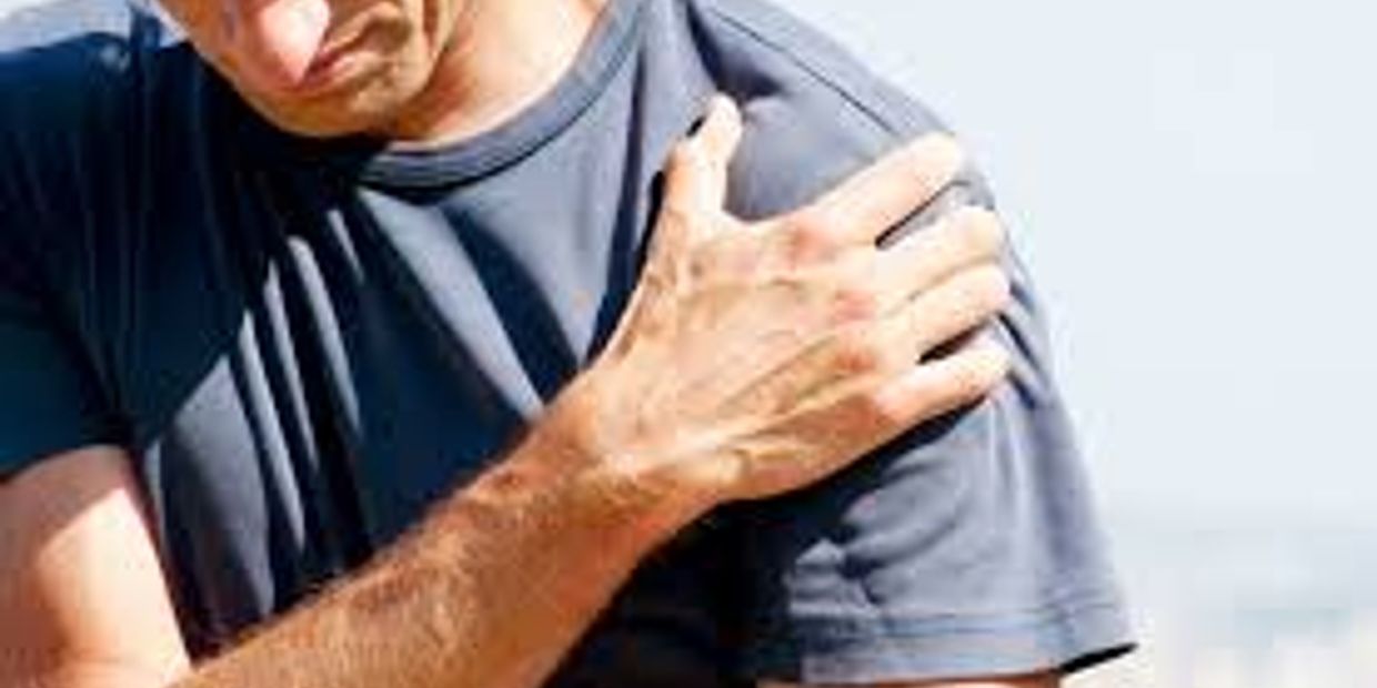 A man in a blue t-shirt looks down and holds his shoulder in pain