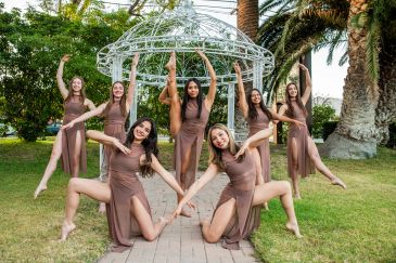 Group of women posing in brown dresses outdoors.