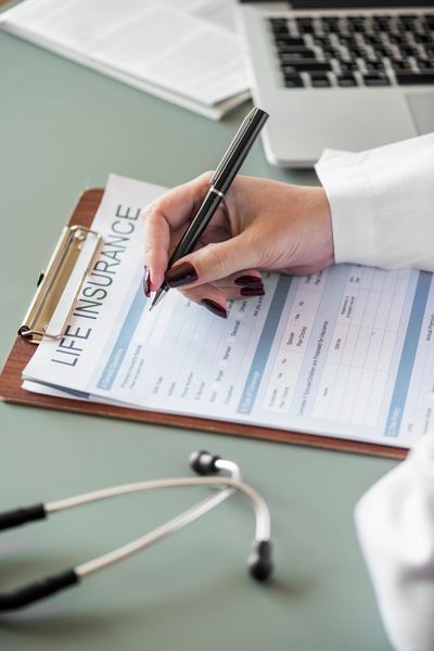 Person filling out a life insurance form with a pen on a clipboard.