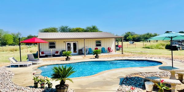 A sunny backyard with a kidney-shaped pool, lounge chairs, and colorful umbrellas.