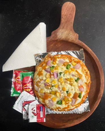 Vegetable pizza on a wooden board with sauces and napkins.
