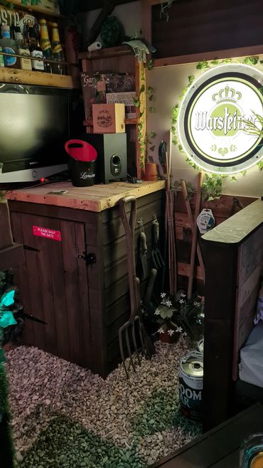 A cozy corner with gardening tools, a TV, and illuminated Warsteiner sign.