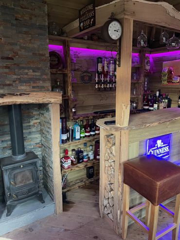 Cozy rustic home bar with wood stove and purple LED lighting.