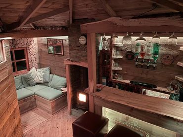 Cozy wooden home bar with cushioned seating and warm stove light.