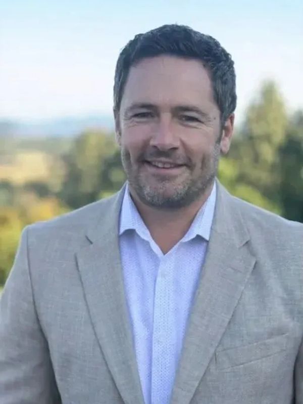 Man in light gray suit jacket smiling outdoors.