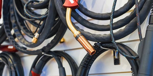 Coiled welding cables and a copper welding torch tip hanging on a wall.