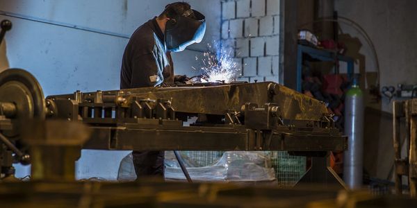 A welder uses a mask while welding metal in a workshop.