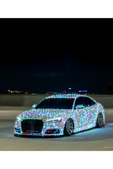 Audi car covered entirely with colorful Christmas lights at night.