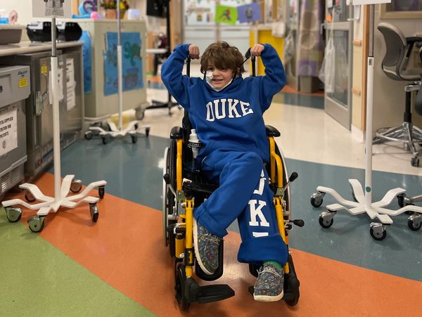Child in a wheelchair smiling under a 'BYE EJ' banner in a hospital.