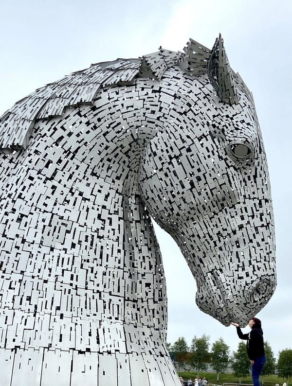 A giant metallic horse head sculpture with a person touching its nose.
