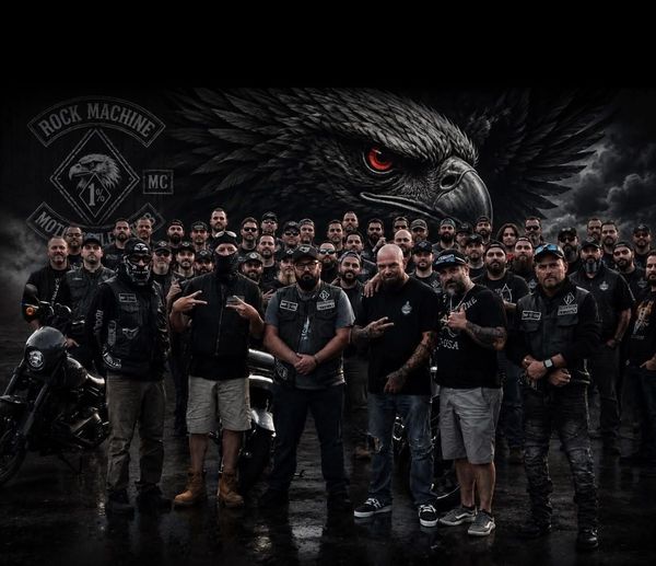 A large group of bikers in black posing with motorcycles and a giant eagle artwork.