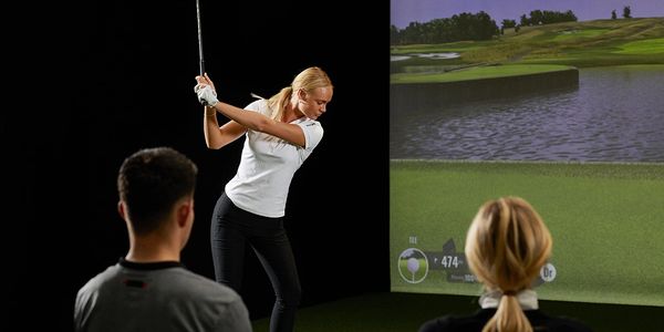 A woman practicing golf swing at XDrive365 indoor golf simulator with friends.