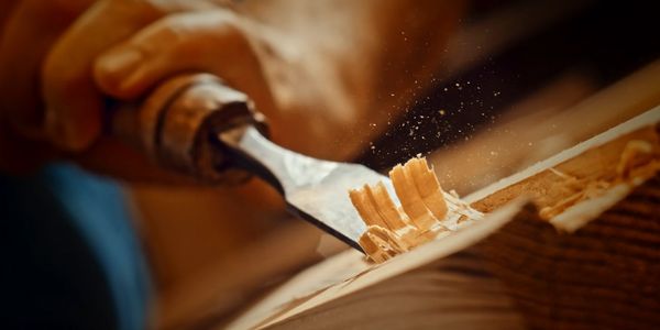 Close-up of hand carving wood with a chisel, creating fine shavings.