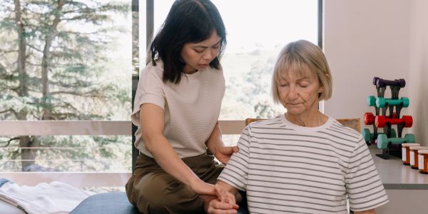A woman helping an elderly lady with arm exercise.