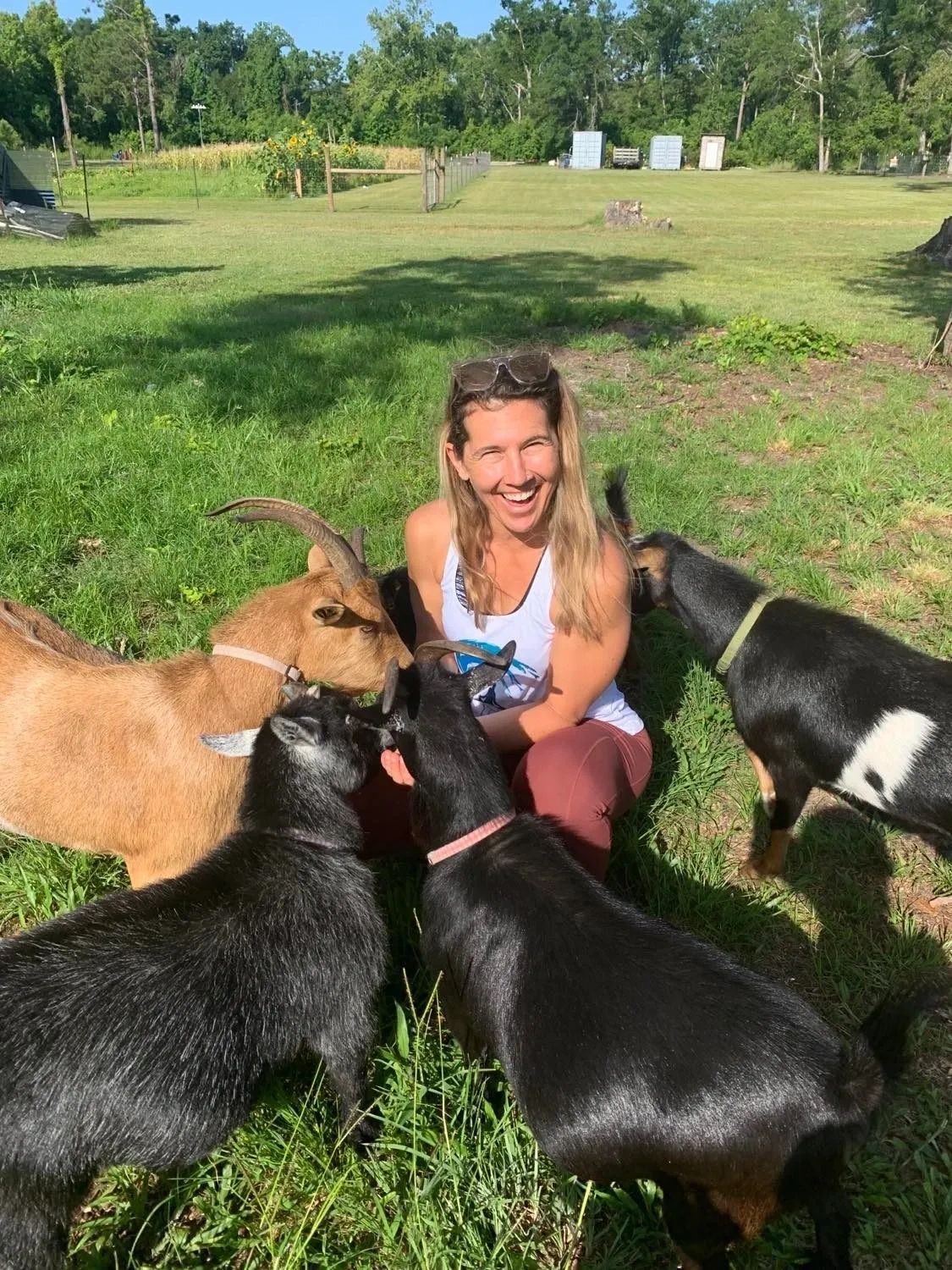 The photo shows a woman kneeling down and playing with goats during a goat yoga session. 