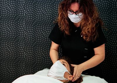 A masked body worker massages the scalp of a masked client.