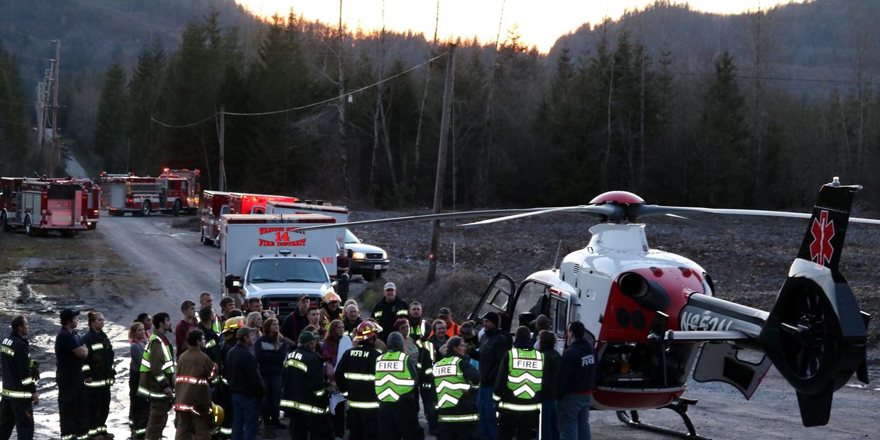 Large group of firefighters training with an Airlift Northwest Helicopter with fire trucks in the ba